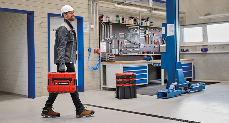 A man carries a toolbox through a workshop