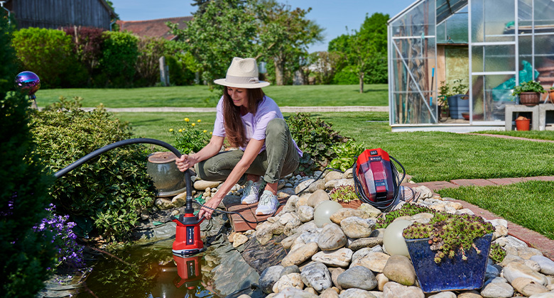 A woman holds a pump in a garden pond.