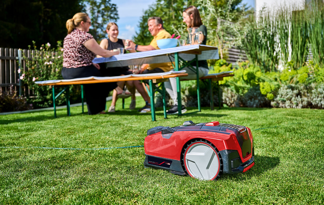 a Einhell robot mower in front of a group of people, sitting on a table; focus on magnetic band