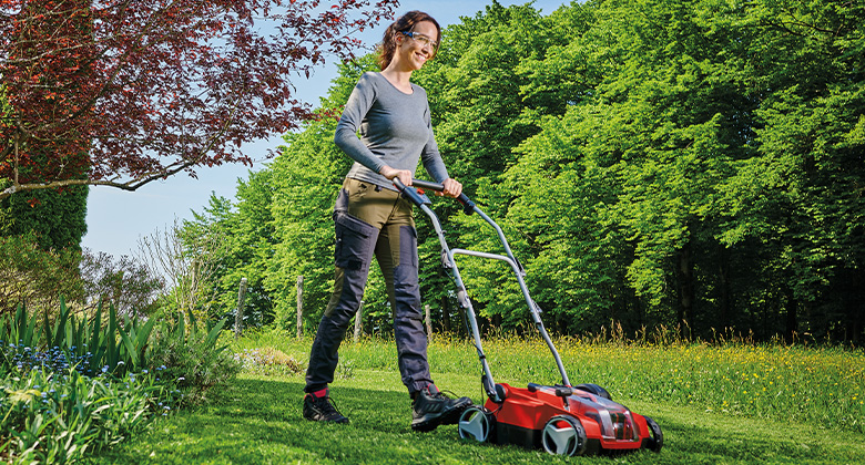 A woman using a einhell scarifier in a well-maintained garden to aerate the lawn and remove moss.