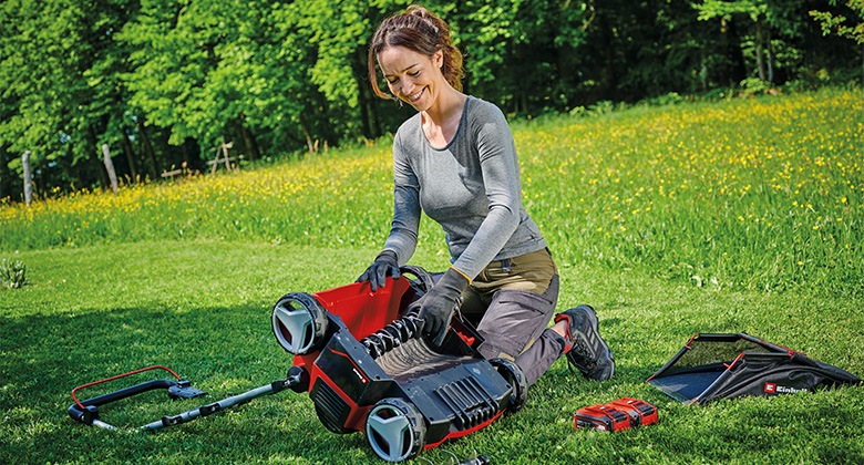 A woman kneeling on the lawn, changing the roller of a einhell scarifier with various tools and accessories beside her.
