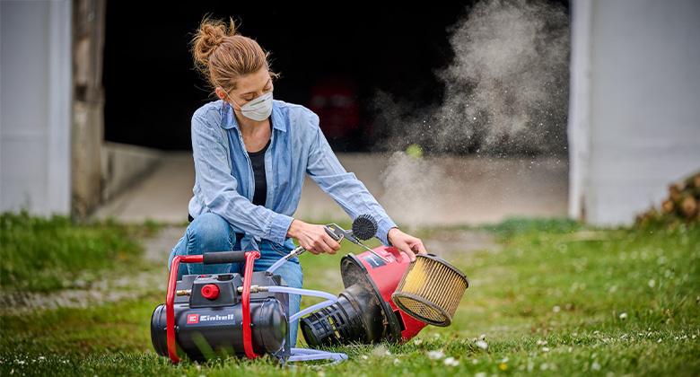 A woman cleans a dirty filter element using an Einhell compressor and a blow gun.
