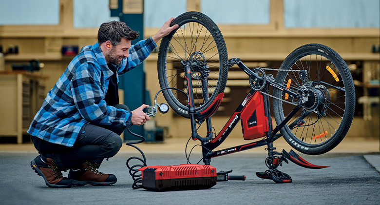 A man uses an Einhell compressor to inflate a bicycle in a workshop.