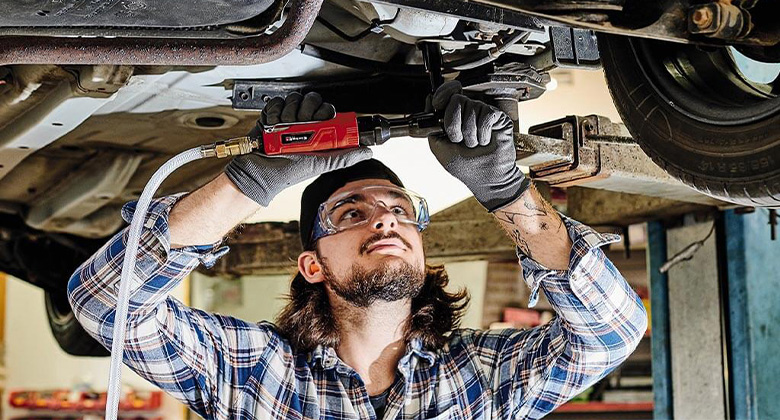 Close-up of a mechanic working under a car with an Einhell die ratchet screwdriver.