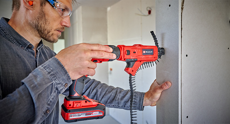 A craftsman screws a drywall panel to a wall using an Einhell cordless drywall screwdriver.