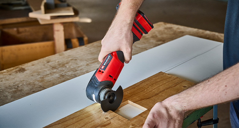 A person uses a Einhell multi-tool to cut a precise rectangle into a piece of wood.