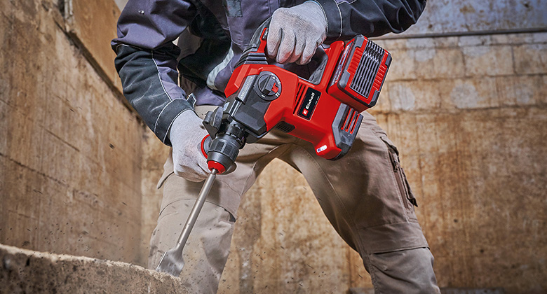 A worker uses a Einhell cordless rotary hammer with a chisel attachment to break concrete.