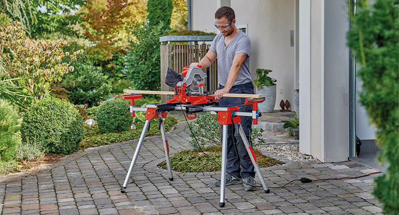 Man using an Einhell miter saw outdoors on a portable workbench.