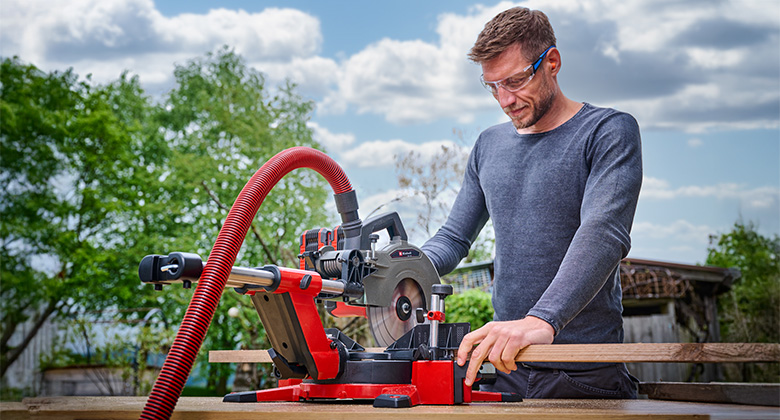 Man working outdoors with an Einhell miter saw connected to a vacuum cleaner.