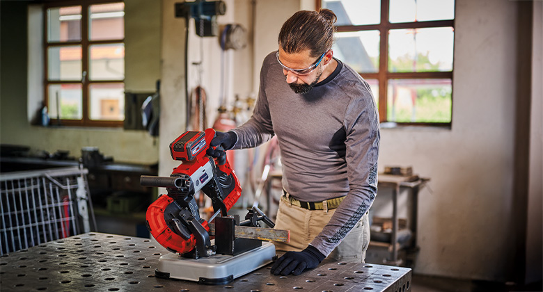 Man cutting metal with an Einhell band saw in a workshop.