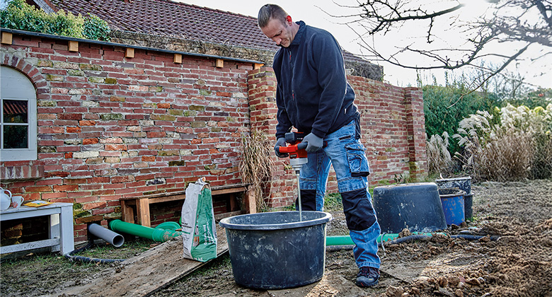 A person uses a mixer to stir material in a bucket in a garden.