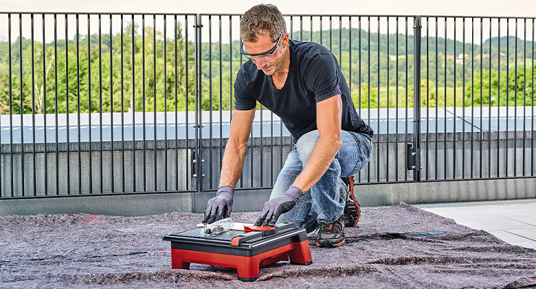 A man cuts a tile with a compact and cordless tile cutter on a rooftop terrace.