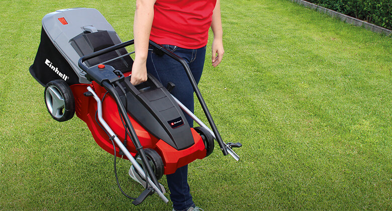A woman carrying a folded Einhell electric lawnmower.