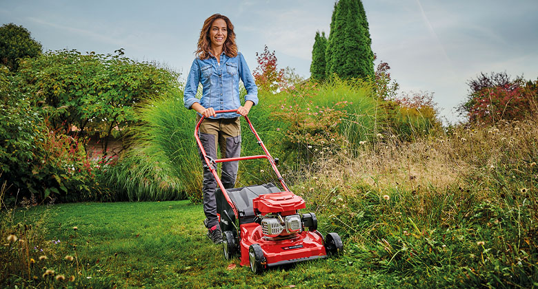 A woman mowing a large lawn with the help of a petrol lawnmower with wheel drive.