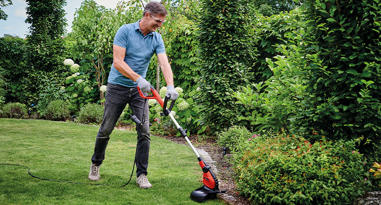 A man cuts the grass in the garden with the help of an Einhell lawn trimmer.