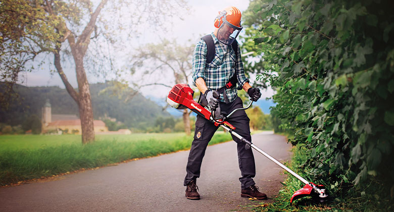 A man cuts tall grass with a petrol scythe from Einhell