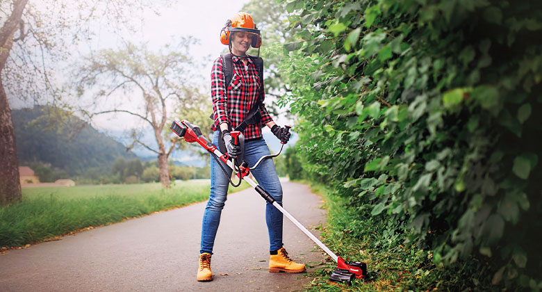 A woman cuts tall grass with a battery-powered scythe from Einhell