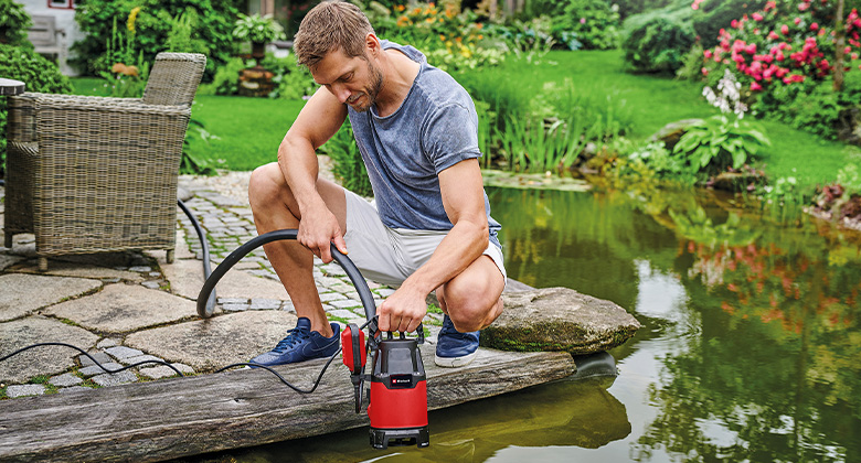 A man placing a dirt water pump in a pond.