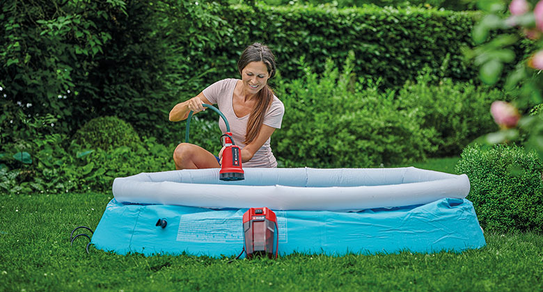 A woman pumping out a pool in a garden using a cordless clear water pump.