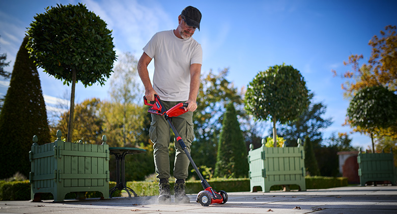 A man cleans paving joints on a patio in a garden using the Einhell cordless patio cleaner.