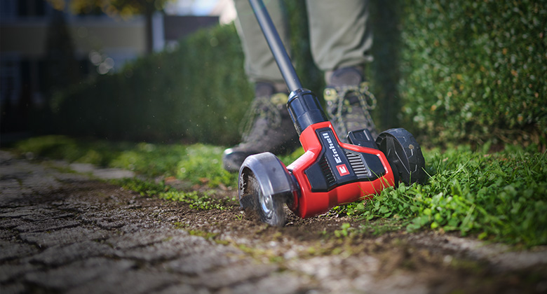 The Einhell cordless patio cleaner removes weeds from paving joints along a garden path.