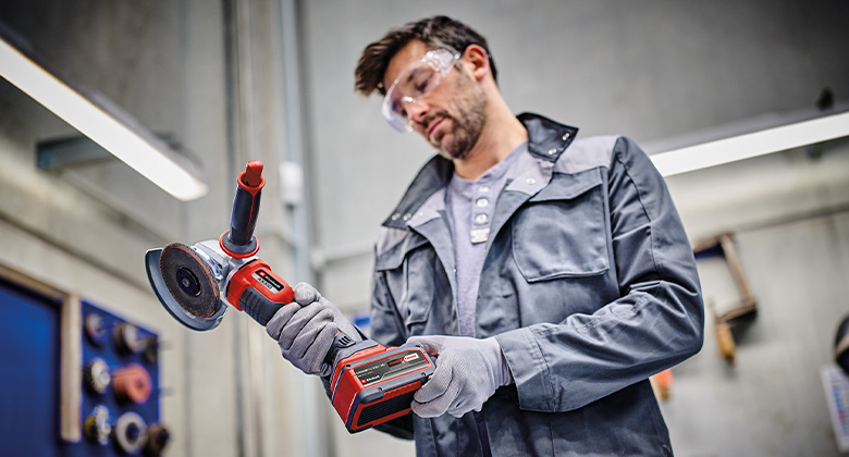 A man inspecting a cordless angle grinder in the workshop.