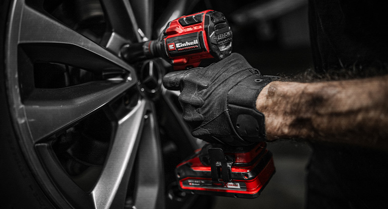 A person uses a cordless impact wrench to tighten or loosen a screw on a car tire.