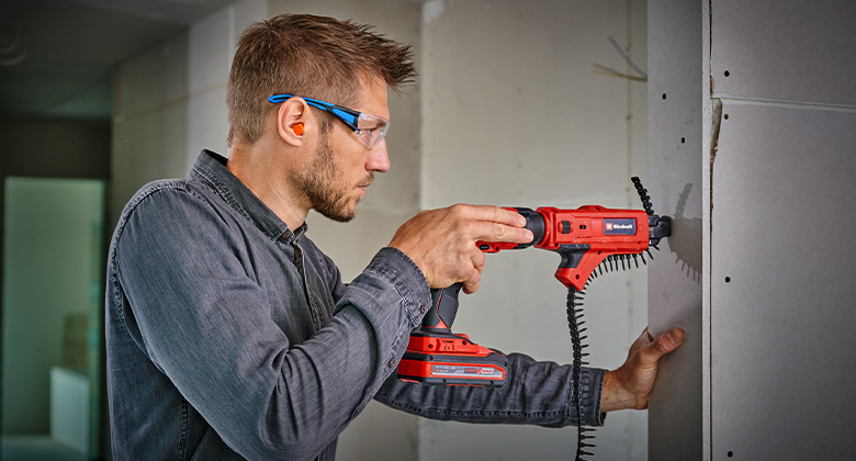 A person uses an cordless drywall screwdriver to fasten screws into a wall.