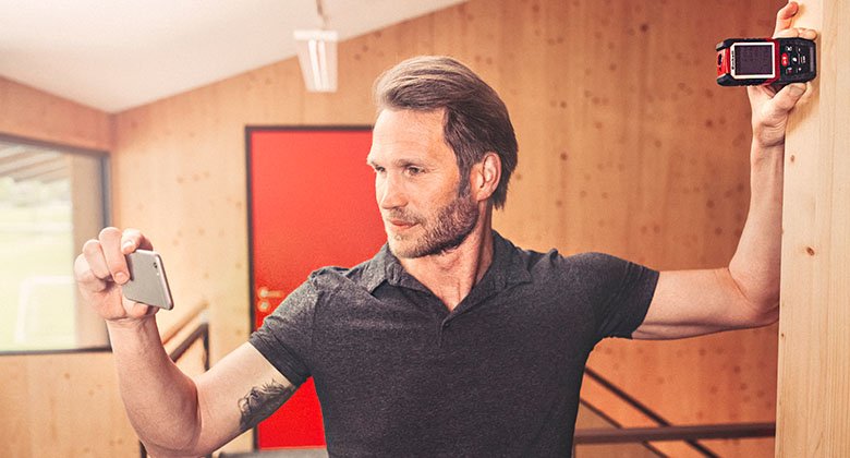 man measuring the wall with the help of a mobile phone and a measuring tool