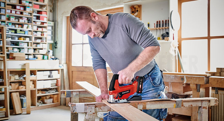 Man in a workshop sawing wood with a jigsaw