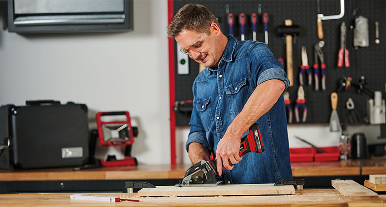man working in a workshop with a cordless mini circular saw